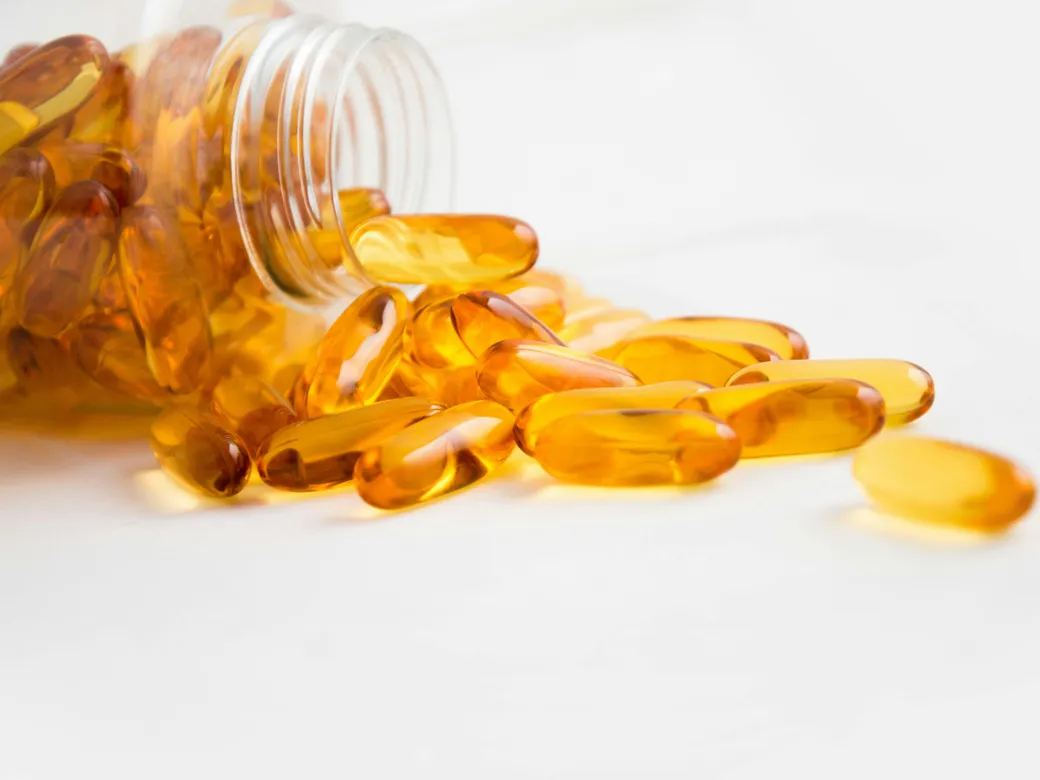 Golden softgel capsules spilling from an open supplement bottle